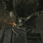 Arbetare med skyddshandskar använder en vinkelslip för att bearbeta metall i en verkstad – gnistor flyger från slipskivan mot det mörka verkstadsgolvet